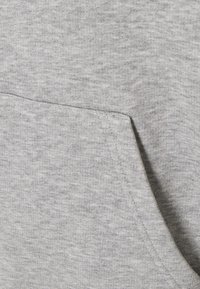 Ljusgrå huvtröja i tyg med en strukturerad mönster och en framficka med sydda kanter, som visar en mjuk och varm känsla.