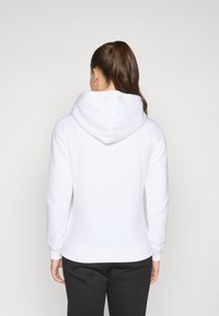Haut à capuche blanc avec une capuche spacieuse, des manches longues et des poignets côtelés. Le tissu semble doux et lisse, adapté pour un usage décontracté.