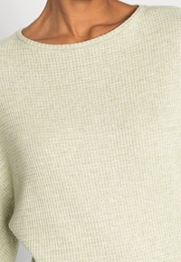 Lichtgroene, geribbelde gebreide trui met een wijde halslijn en zachte textuur, kort bij de schouders voor een ontspannen pasvorm.