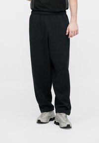 Μαύροι φορμάκια από μαλακό ύφασμα με ελαστική μέση και στενές κάτω μπροστά, συνδυασμένοι με αθλητικά παπούτσια ανοιχτού γκρι χρώματος.