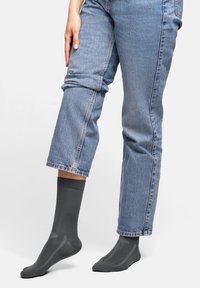 Grå ankelsockar i ett slätt stickat material, med en kontrasterande ribbad mudd och subtila randiga detaljer, tillsammans med ljusblå denimjeans.