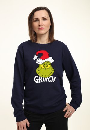 Marineblaues Sweatshirt mit einem Cartoon-Grinch-Design, der einen roten Weihnachtsmannhut mit weißem Fellbesatz trägt, darunter großer weißer Text "GRINCH".