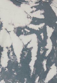 T-shirt tie-dye avec des motifs blancs et gris, avec le texte brodé "A TRIP ABROAD" sur la poitrine.