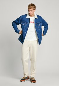 Denim jakker valge sherpa kraega, nööpidega ees, kaks rinna taskut, kombinatsioon valge T-särgi ja kreemikate pükstega.