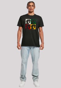 Black t-shirt with a graphic of four stylized faces, featuring green, red, yellow, and white backgrounds. Soft cotton fabric, relaxed fit.