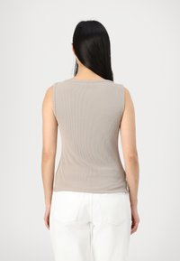 Top sans manches beige en maille côtelée avec un col rond, présentant une texture subtile. Associé à un pantalon blanc taille haute, vu de dos.
