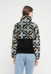 Μαύρο και μπλε φλις μπουφάν με σχέδιο λουλουδιών, ψηλό γιακά και υφή υφάσματος. Διαθέτει μια μονή μαύρη περιοχή στο κάτω μέρος.