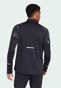 Zwarte sportieve longsleeve shirt met tekstuurschouders, reflecterende accenten en een kwart rits. Glad materiaal en strak ontwerp.
