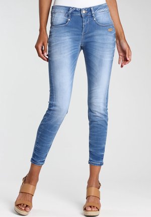Jean skinny bleu clair délavé porté avec des sandales à plateforme marron clair, montré de la taille aux chevilles sur un fond neutre.
