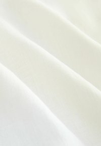 Bílá lněná tkanina s jemnou texturou, zdobená něžnými záhyby a subtilním vzorem tkaní, který zdůrazňuje její lehkost a prodyšnost.