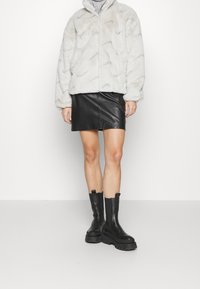 Světlá šedá kabátek z umělé kožešiny, volnější střih, se zipem. Černá kožená mini sukně, spárovaná s robustními černými kotníkovými botami.