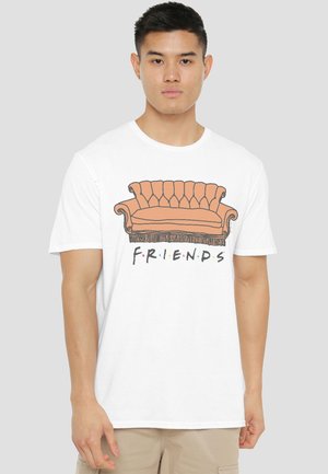 Young man wearing white t-shirt with orange couch and "FRIENDS" text featuring colored dots on a light gray background.