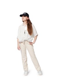 Wit gestreepte shirt geknoopt om de taille, beige broek en een zwarte pet. Witte sneakers met zilveren accenten maken de outfit compleet.