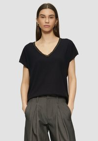 Musthave mustiga V-kaelusega T-särk, millel on lühikesed varrukad ja pitsäärisega kaelus. Ühendatud hallide pinstripe pükstega.