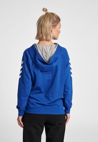 Felpa con cappuccio blu e fodera grigia, con strisce bianche lungo le maniche e una vestibilità comoda. Tessuto morbido e polsini a coste.