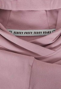 Różowa bluza z miękkiego materiału, z ribbanym wykończeniem rękawów i metką z napisem "PUCHATE PUCHATE MISIE" wszytą w dekolt.