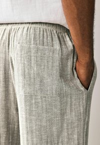 Pantaloni din in gri deschis, cu un design texturat și cu nervuri, având buzunare laterale și un mânecă elastică pentru confort.