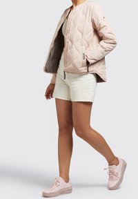 Light pink quilted bomber jacket with a zip closure and two side pockets, paired with cream shorts and matching light pink sneakers.
