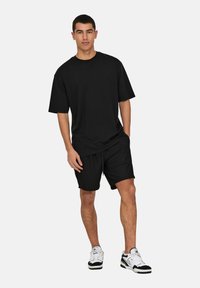 Camiseta de algodón negra de corte relajado, combinada con pantalones cortos negros a juego. Presenta mangas cortas y un escote redondo. Zapatillas casuales completan el look.