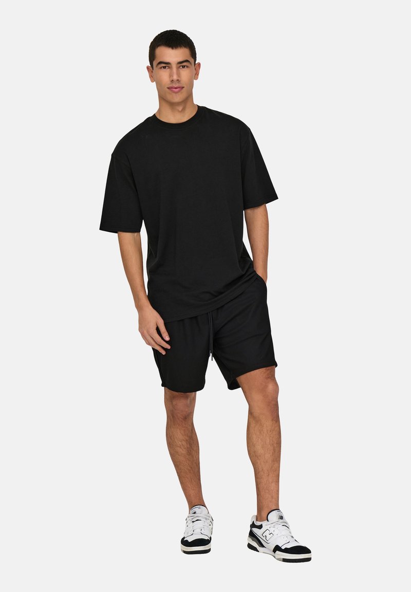 Svart bomullströja med avslappnad passform, matchad med svarta shorts. Har korta ärmar och rundad halsringning. Avslappnade sneakers fulländar looken.