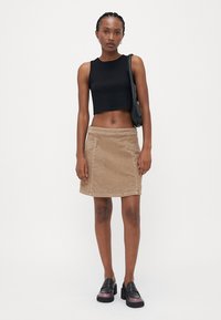Débardeur noir court, jupe mini en velours côtelé beige avec poches latérales, tissu texturé et finition lisse ; associée à des chaussures à plateforme noires.