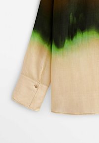 Chemise à manches longues beige avec un motif de teinture dégradée vert et noir sur le haut du bras et le poignet, fermeture par bouton.