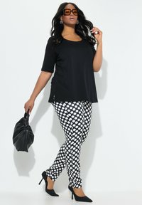 Zwarte top met korte mouwen en strakke zwart-witte polkadot leggings. Model houdt een zwarte tas vast en draagt zwarte hakken en grote bruine zonnebrillen.