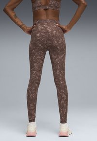 Leggings marron à motif marbré avec une taille haute, confectionnés dans un tissu texturé, associés à des chaussures de sport claires.