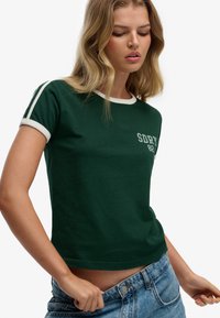 Groen cropped T-shirt met witte kraag en mouwaccenten, met het logo "SDRY 82". Materiaal lijkt zacht met een aangesloten pasvorm.