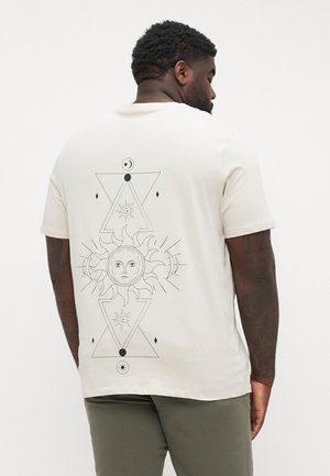 T-shirt en coton beige avec un graphique géométrique noir représentant un soleil et une lune au dos, avec des éléments triangulaires et un travail de ligne détaillé.