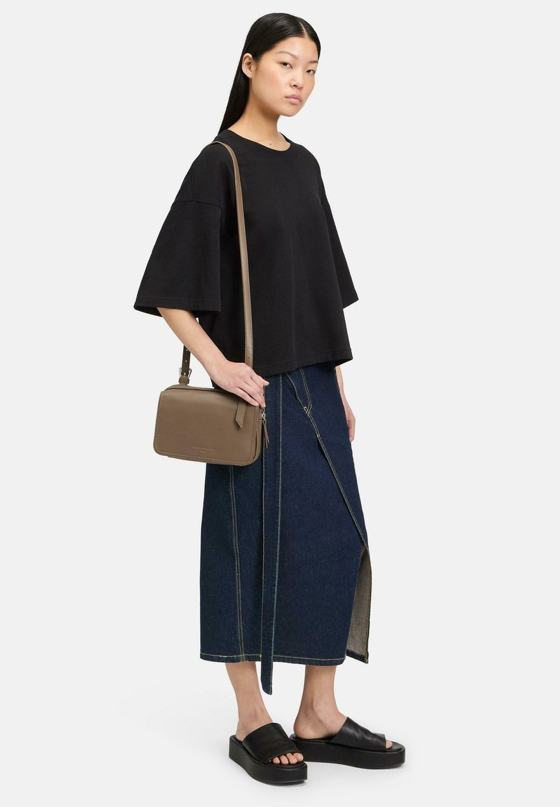 Schwarzes Übergröße T-Shirt, dunkelblaue Jeansrock mit seitlichem Schlitz und gelben Nähten, braune Umhängetasche, schwarze Plateausandalen.