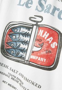 Koszulka z grafiką przedstawiającą puszkę w czerwono-niebieskich kolorach, z rybami w środku. Tekst zawiera "Le Sard." oraz "Świeże, Słone i Wędzone."