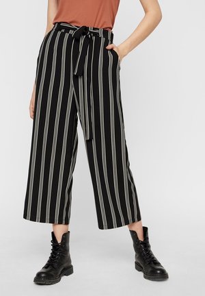 Mujer con pantalones anchos cortos de rayas verticales en blanco y negro, con un cinturón anudado y botas negras con cordones.