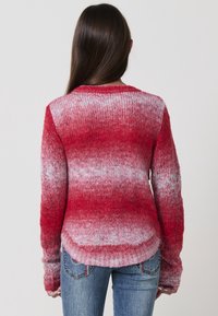 Maglione lavorato a maglia rosso e bianco con effetto ombre, maniche lunghe, scollatura rotonda e orlo a costine. La texture è pelosa e spessa, adatta per il clima più freddo.
