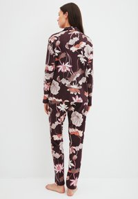 Floral pyjamapakket in donkerpaars, met lange mouwen en broek. Zachte stof met roze en beige accenten, details op kraag en manchetten.