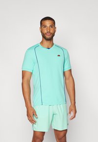 Light blue athletic shirt with short sleeves and a v-neck, featuring contrasting navy blue stitching and a logo on the chest.
