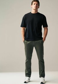 Black short-sleeve t-shirt paired with olive green slim-fit pants and white athletic shoes. Simple, modern design with clean lines.