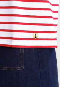 T-shirt a maniche corte a righe rosse e bianche con un logo di ancora giallo sull'orlo, abbinato a jeans in denim scuro con una tasca posteriore.
