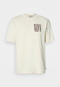 Μπλουζάκι από βαμβάκι σε κρέμ χρώμα με στρογγυλή λαιμόκοψη. Διαθέτει γραφιστικό σχέδιο σε μοβ και πράσινο στην αριστερή πλευρά του στήθους. Κοντά μανίκια.