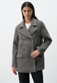 Cappotto grigio in lana a doppio petto con rever, quattro bottoni, tasche laterali e vestibilità sartoriale. Texture liscia con dettagli cuciti.