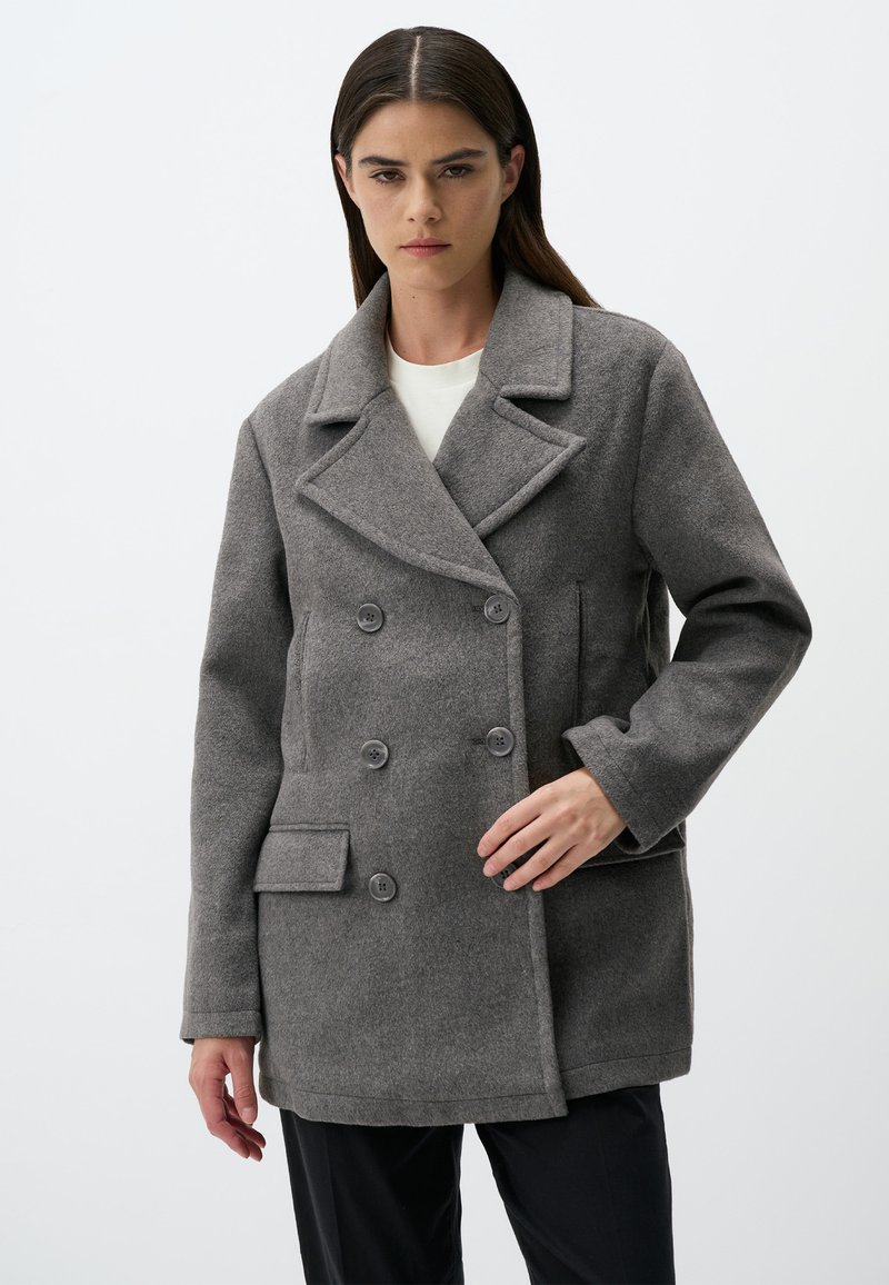 Cappotto grigio in lana a doppio petto con rever, quattro bottoni, tasche laterali e vestibilità sartoriale. Texture liscia con dettagli cuciti.
