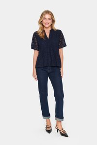 Mere pitsidega õhuline lahtine alläärige ja V-kaelusega tumesinine pitsi topp, millele on kombineeritud kahekohalised tumehallid džinsid ja mustad rihmatuurikesed kontsad. Sile ja tekstuuriga välimus.