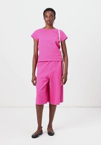 Rosa bomulls to-delt antrekk med kortermet topp og knelengde shorts. Glatt tekstur med en avslappet passform, parret med svarte leiligheter.