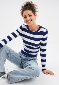 Blau-weiß gestreifter gerippter Pullover mit Rundhalsausschnitt, kombiniert mit hellblauen weit geschnittenen Jeans und weißen Sneakers.
