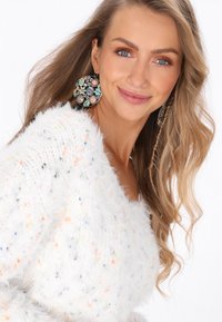 Weißer flauschiger Pullover mit mehrfarbigen Sprenkeln, kombiniert mit großen Ohrringen im Blumenmuster mit blauen, rosa und gelben Akzenten.