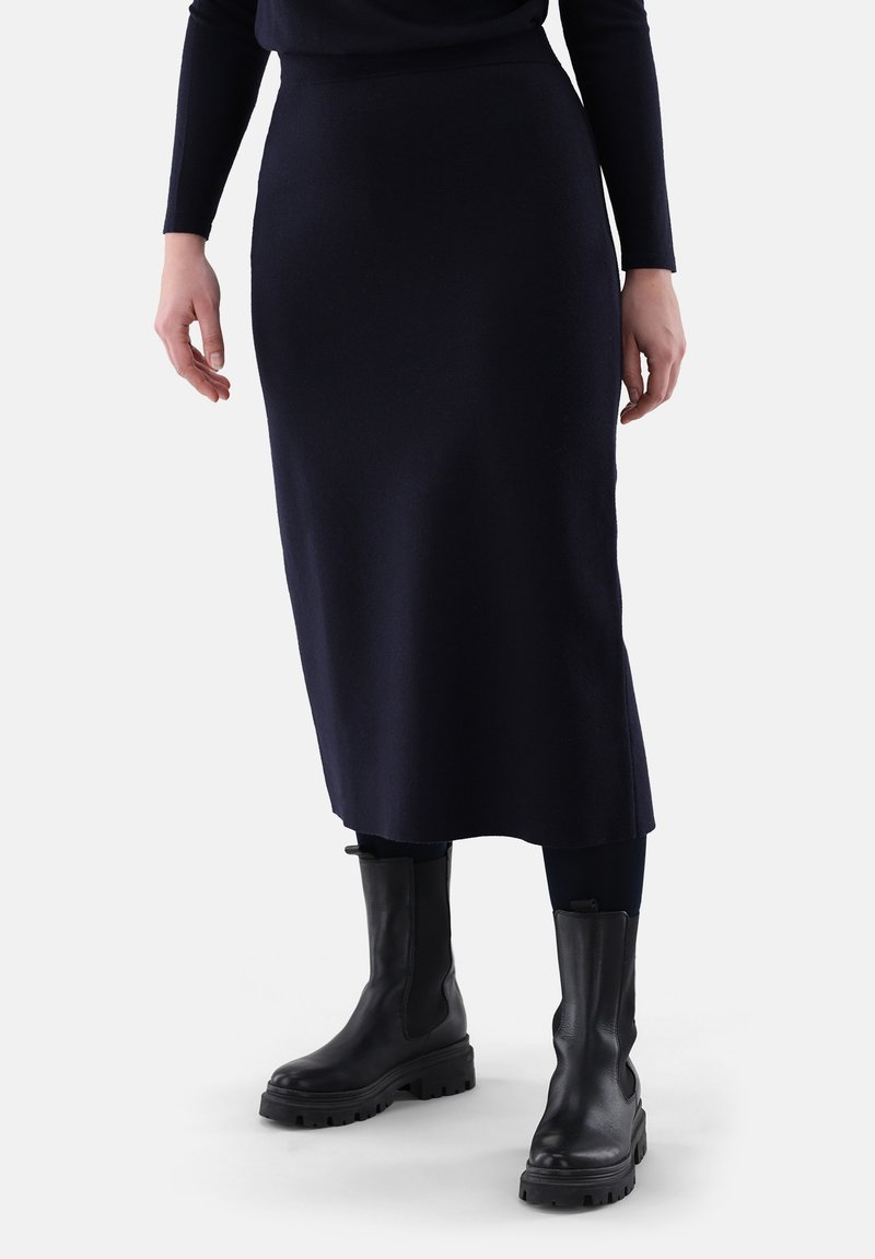 Mittelkurzer, marineblauer Strickrock mit glatter Textur und nahtlosem Design, kombiniert mit schwarzen Stiefeletten mit einer klobigen Sohle.