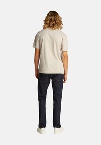 T-shirt in cotone beige chiaro con maniche corte abbinato a jeans in denim blu scuro. Le scarpe sono bianche con una finitura liscia.