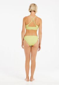 Zelený pruhovaný bikini set s topem na kříž a prořezávaným detailem a odpovídajícími nízkými kalhotkami. Hladká textura, minimalistický design.