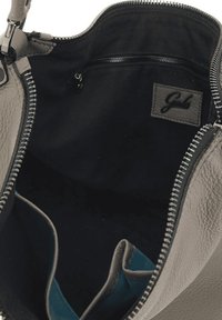 Sac à main en cuir gris avec un intérieur en tissu noir. Dispose d'une fermeture éclair, de poches internes et d'une étiquette de logo.