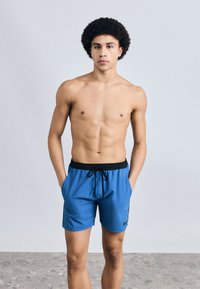 Μπλε μαγιό σορτς με μαύρο κορδόνι στη μέση, πλαϊνές τσέπες και λογότυπο. Λείο ύφασμα, μήκος μέχρι τη μέση του μηρού, κανονική εφαρμογή.